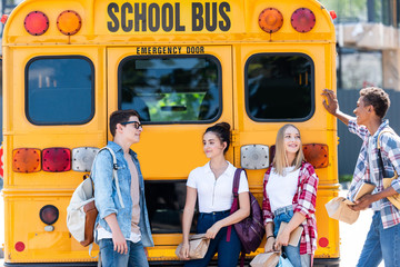 group of teen scholars chatting while leaning on school bus