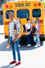 handsome smiling teen schoolboy looking at camera while his classmates standing behind near school...