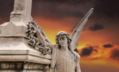 Angel sculpture against the dramatic orange sky in Poblenou Cemetery. Peaceful but macabre, cemetery of Poblenou is today home to incredible sculptures, haunting, yet beautiful.