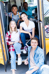 group of teen scholars sitting at school bus with driver inside and looking at camera