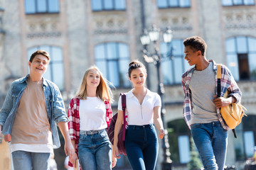 Obraz premium group of happy multiethnic teenagers with backpacks having walk together