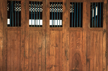 vintage retro wooden doors and window panes with bars, home interior architectural design against plain tropical dark brown textured wood panel board wall in old Asian house