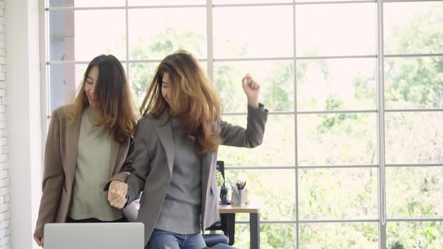 Happy young Asian woman wearing suit dancing while working in her office. Beautiful teenager enjoy and having fun relax at workplace.