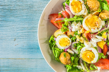 Traditional French countryside lunch - salad with tomatoes, arugula, potatoes and boiled eggs in a plate on rustic wooden table - copy space