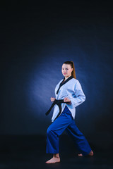 The karate girl in white kimono and black belt training karate over gray background.