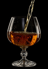 Cognac is poured into a glass, a spray of a drink, on a black background