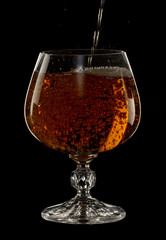 Cognac is poured into a glass, a spray of a drink, on a black background