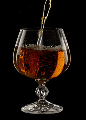 Cognac is poured into a glass, a spray of a drink, on a black background