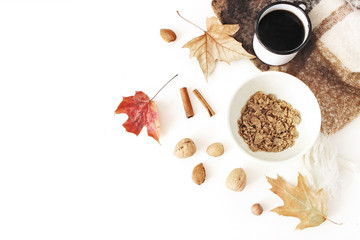 Autumn, fall breakfast composition. Cup of coffee, bowl of oat flakes, muesli, blanket, autumn leaves, cinnamon sticks, almonds and nuts on white table background, flat lay, top view. Vegetarian food.