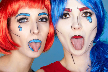 Females in red and blue wigs on blue background. Girls show each other tongues