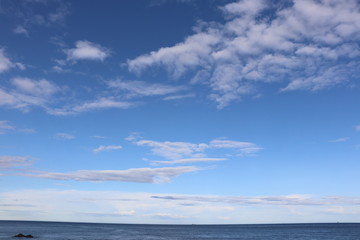 Naklejka na ściany i meble Fluffy white clouds in blue sky over horizon and sea