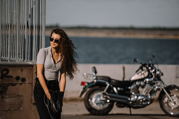 Fototapeta na wymiar beautiful girl in sunglasses posing on quay with cruiser motorcycle on background