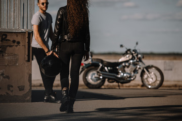Obraz na płótnie Canvas girl holding helmet and going to boyfriend with classical motorbike