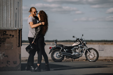 Fototapeta na wymiar young bikers embracing in city with classic motorbike on background