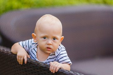 Fototapeta premium A beautiful baby boy walks in the yard holding on to a chair