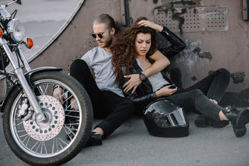 Fototapeta na wymiar couple of bikers hugging and sitting on asphalt with helmet and motorcycle