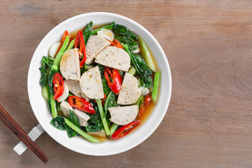 top view of stir fried chinese kale and vietnamese pork sausage with soy sauce in a ceramic dish on wooden table. asian homemade style food concept.