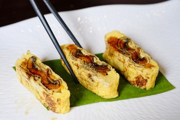 Use chopstick to pick up Japanese egg rolls with Grilled Eel (Unagi) on white plate