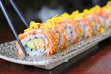 Use chopstick to pick up salmon sushi roll with spicy sauce - japanese food style