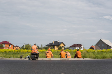 Four workers resting on the road construction site with a houses behind them.