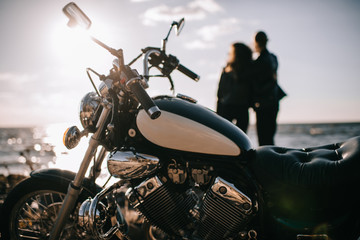 selective focus of classical chopper motorbike and couple looking at sea on background - obrazy, fototapety, plakaty