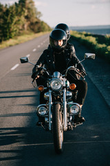 young couple in helmets riding classical motorbike on country road