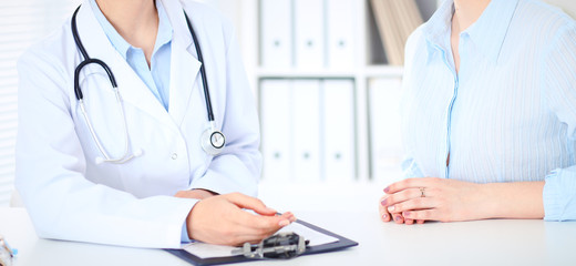 Unknown female doctor and patient discussing something while sitting at the table at hospital. Medicine and healthcare concepts