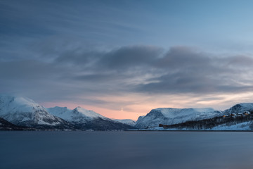 Landscape of a Norwegian fjord and town in winter at sunset.