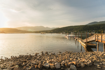 Naklejka premium Scenic Bay at Sunset with a Wooden Pier and a Rochy Shore in Foreground. Port Moody, BC, Canada.