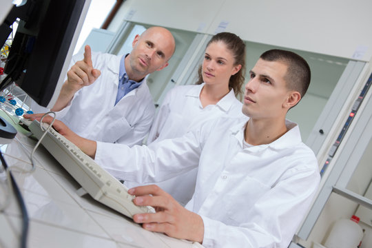 Students and teacher in labcoats loking at computer