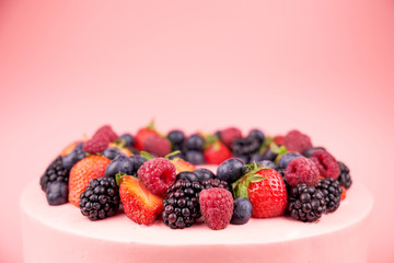 Cake with whipped pink cream, fresh strawberries, blueberries, blackberry and raspberry on pink background. Close up. Picture for a menu or a confectionery catalog.