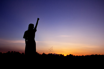 Happy celebrating winning success woman silhouette on sky background.