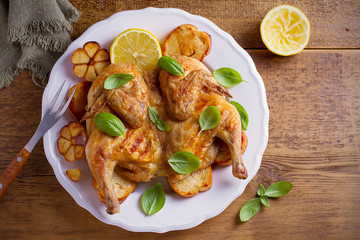 Whole chicken on toasted bread with lemon, basil and garlic on white plate, wooden table. overhead, horizontal