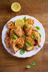 Whole chicken on toasted bread with lemon, basil and garlic on white plate, wooden table. overhead, vertical