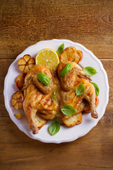 Whole chicken on toasted bread with lemon, basil and garlic on white plate, wooden table. overhead, vertical