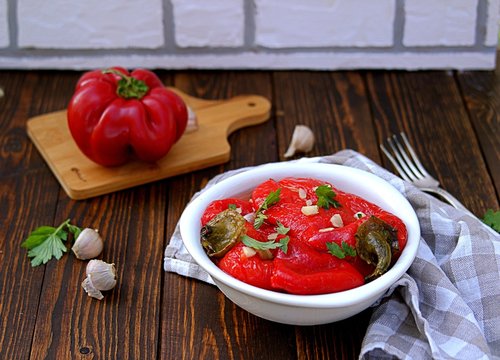 Appetizer, roasted pickled sweet red pepper in a white bowl on a wooden background. Serbian cuisine.