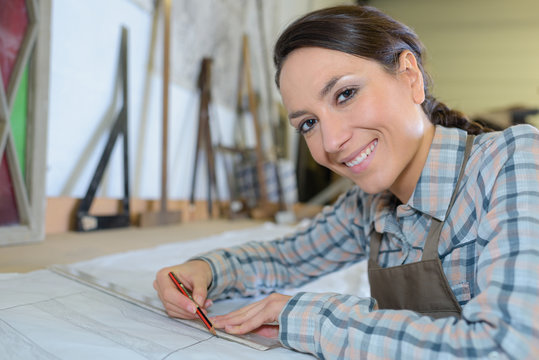 confident female carpenter drawing on blueprint at table in workshop