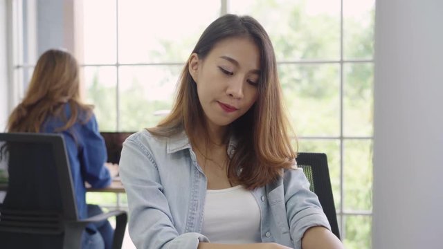 Cheerful asian young businesswoman sitting in office drinking coffee. Attractive asian creative woman holding a cup of coffee while working in workplace.