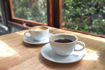 Closeup image of two white cups of hot coffee on wooden table in cafe