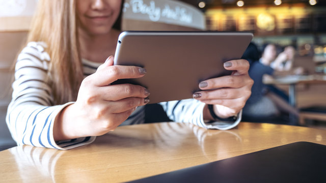 Closeup image of an asian woman holding , looking and using tablet pc in modern cafe