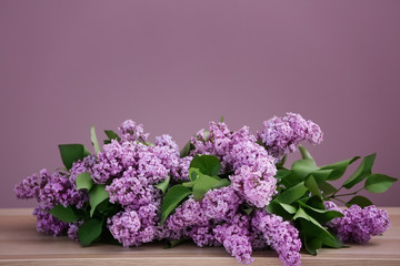 Beautiful blossoming lilac on table against color background