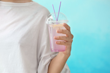 Woman holding plastic cup with fresh lavender lemonade on color background, closeup