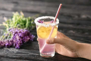 Woman holding glass with fresh lavender lemonade on wooden background, closeup