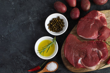 Fresh raw meat beef steak olive oil Uncooked potato Spices Salt Wooden spoon Chili Pepper Rosemary Cooking concept Cooking concept Dark concrete background Top view Copy space Flat lay