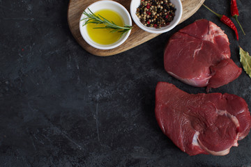 Fresh raw meat beef steak olive oil Spices Salt Wooden spoon Pepper mix Rosemary Bay leaf Cooking concept Cooking concept Dark concrete background Top view Copy space Flat lay