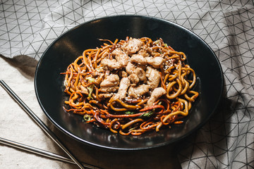 Meat with noodles in black plate, Asian cuisine, chopsticks