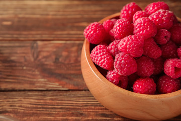 Bowl with fresh ripe raspberries on wooden table, closeup
