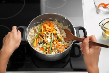 Woman cooking tasty rice with vegetables in kitchen