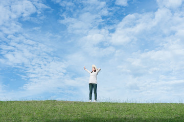 Standing woman raised her hands on the mountain, natural green and beautiful sky.