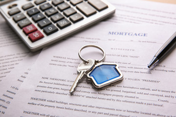 Key with trinket, pen and calculator on mortgage contract